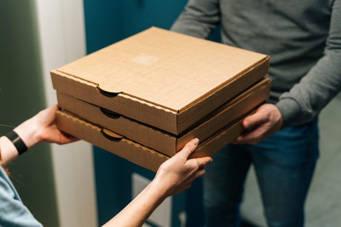 Close-up of female customer receiving pizza boxes with takeaway at home from delivery man hands