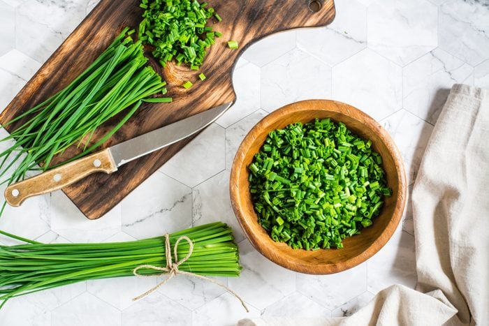 Fresh chopped green onions in a wooden bowl and a cutting board on the table. Top view