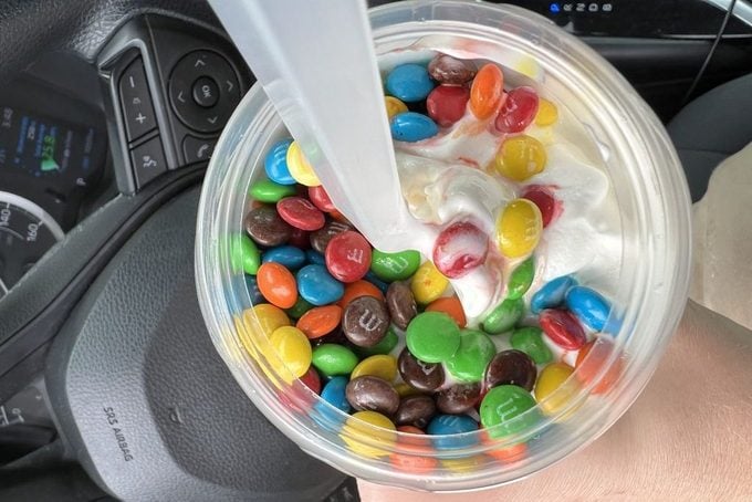Closeup of M&M Mcflurry in a vehicle against a steering wheel and the driver cockpit