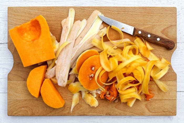Cut up butternut squash with peels and knife on brown wood chopping board isolated on white from above.