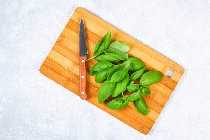 basil on a wooden cutting board with a knife to the side