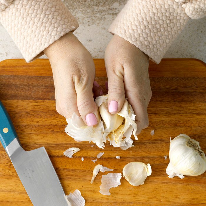 Hands Breaking Off Many Cloves With Knife On Cutting Board