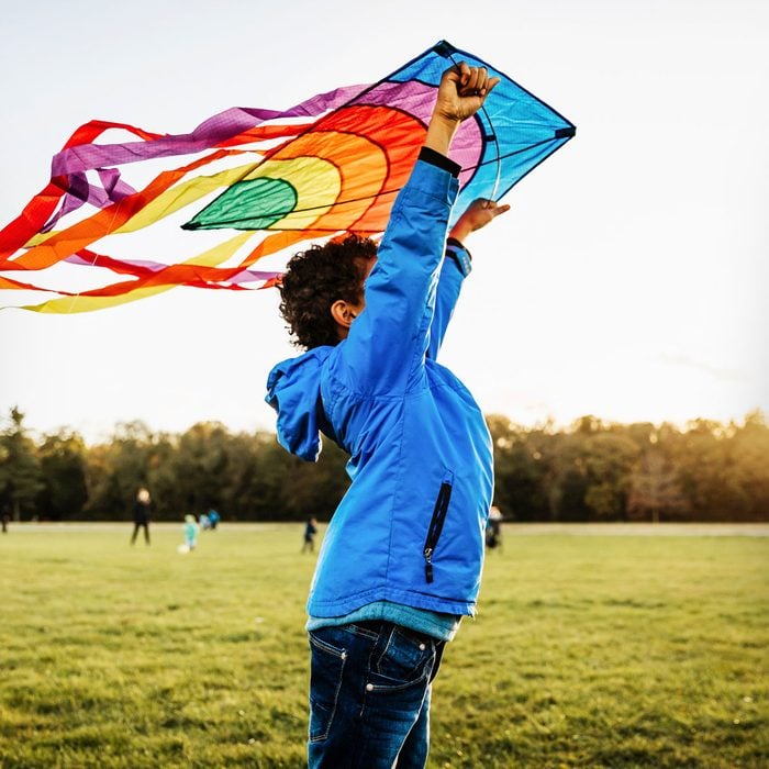 A Young Boy Out In A Park Learning To Fly A Colourful Kite