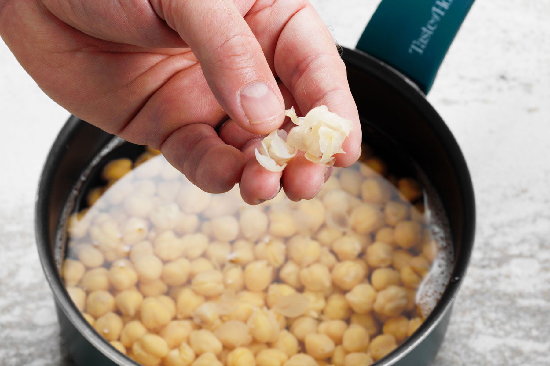 A person removing the skins from a chickpea to make homemade hummus.
