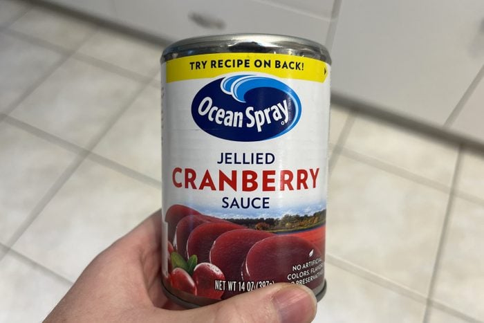 Person's hand holding a container of Ocean Spray jellied cranberry sauce