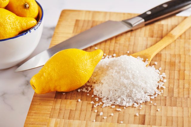 lemon and salt on a wooden cutting board with a knife and wooden spoon in the background