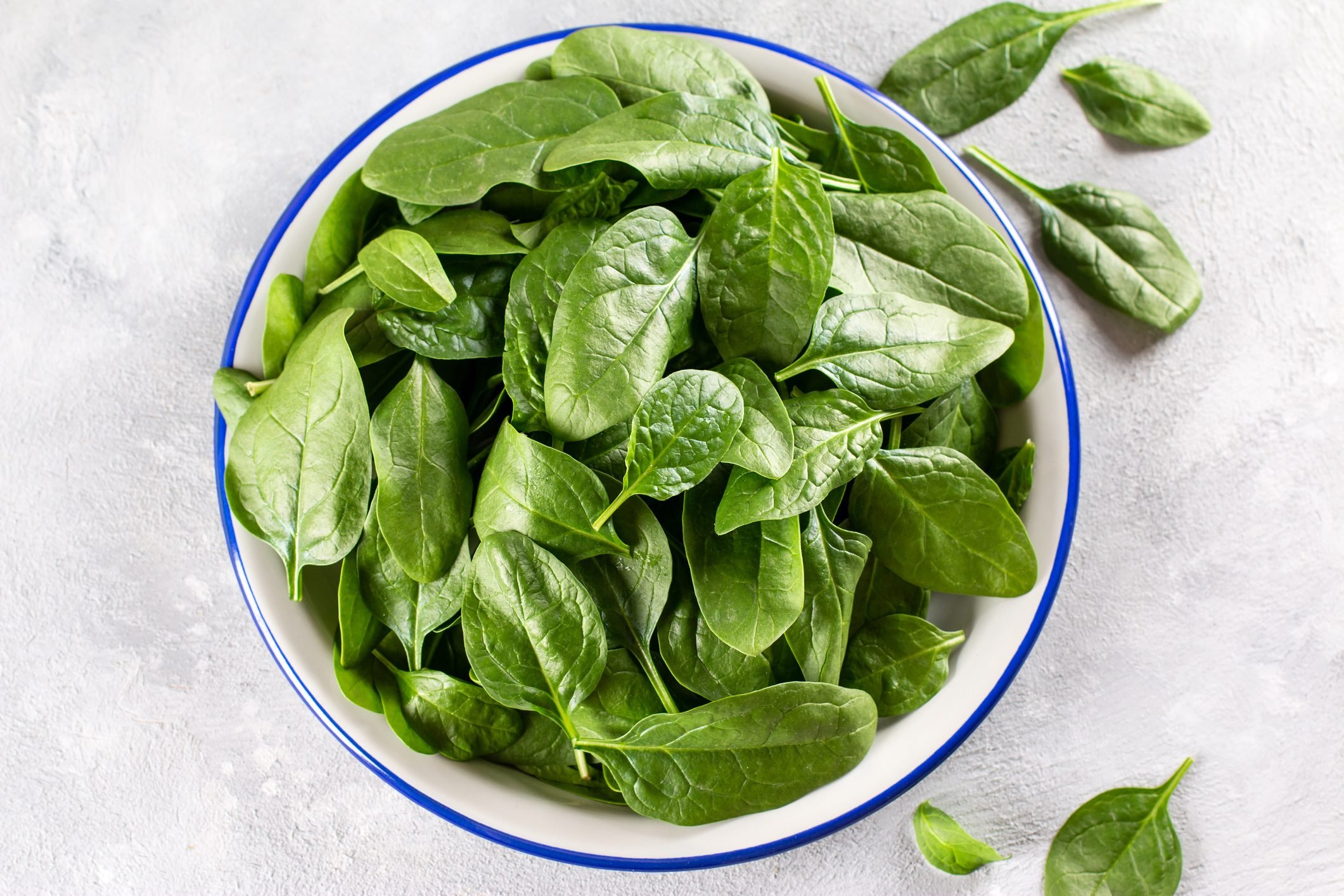Fresh organic baby spinach leaves on a plate on a light concrete background, top view. Healthy food concept.