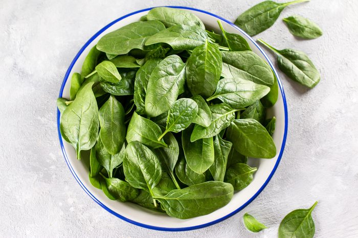 Fresh organic baby spinach leaves on a plate on a light concrete background, top view. Healthy food concept.