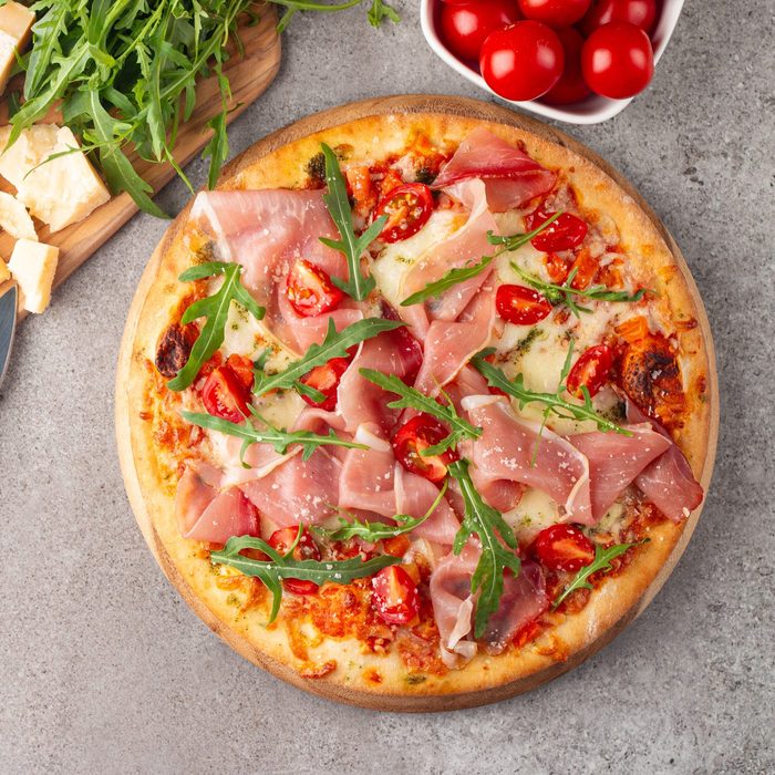Pizza with prosciutto, ham, arugula, tomatoes, pesto, cheese and parmesan. Italian cuisine.