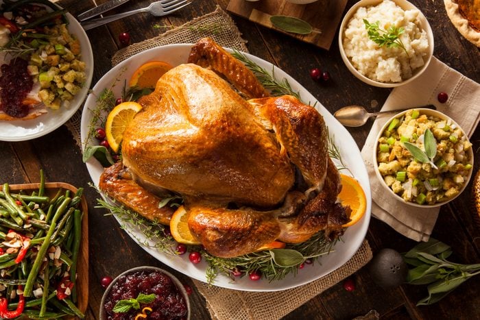 Overhead of Whole Homemade Thanksgiving Turkey with homemade sides like stuffing, mashed potatoes, green beans and more displayed on a wooden family kitchen table