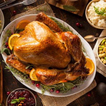 Overhead of Whole Homemade Thanksgiving Turkey with homemade sides like stuffing, mashed potatoes, green beans and more displayed on a wooden family kitchen table