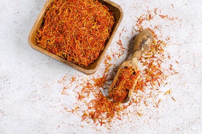 dry saffron spice in a wooden bowl with a wooden spoon on a stone background