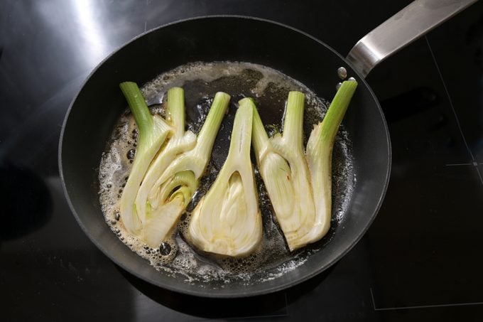Fresh fennel slices are fried in butter in a cooking pan on a black stove, preparation for an healthy vegetarian meal, selected focus