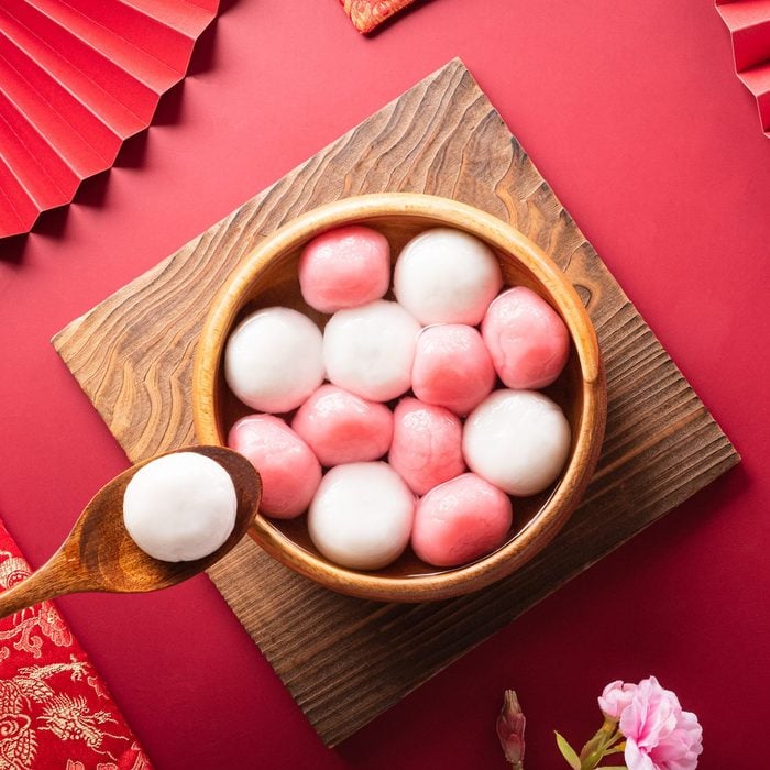 Tang Yuan(sweet dumplings balls), a traditional cuisine for Mid-autumn, Dongzhi (winter solstice ) and Chinese new year with plum flower and tea on red background.