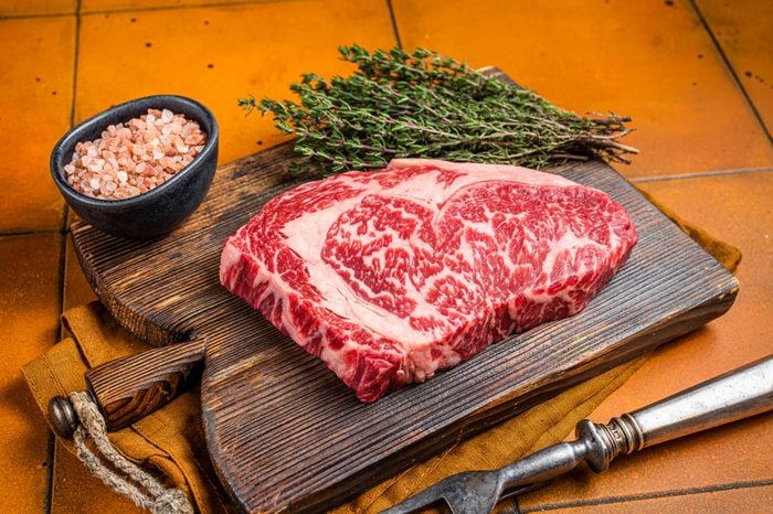 Prime Raw wagyu Rib Eye beef meat steak on wooden board. Orange background. Top view