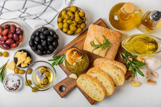 Italian ciabatta bread cut in slices with herbs, olives, pesto sauce, garlic and parmesan cheese on a concrete table. Fresh homemade Italian Ciabatta bread sliced with herbs and spices.Place for text.