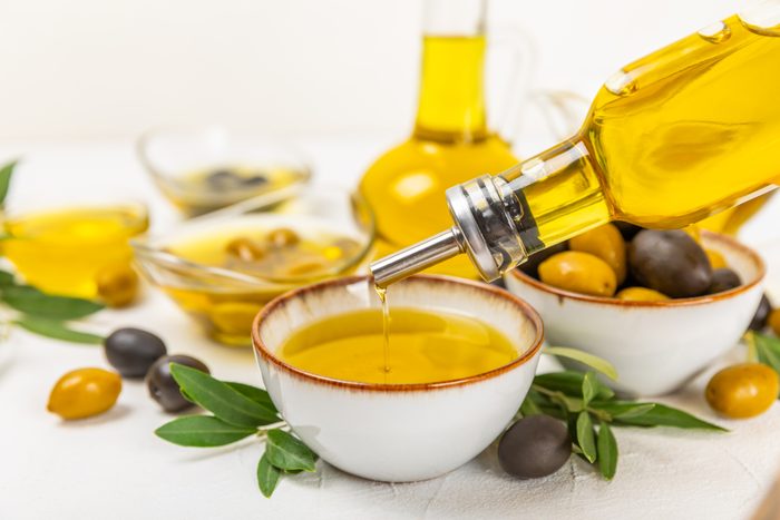 Olive oil in a bottle and gravy boat on the kitchen table. Oil bottle with branches and fruits of olives. Place for text. copy space. vegetable oil and salad dressing.