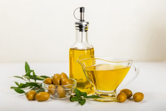 Olive oil in a bottle and gravy boat on the kitchen table. Oil bottle with branches and fruits of olives