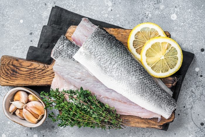 Fresh Raw Sea Bass fillets, Branzino fish with thyme and lemon. Gray background. Top view