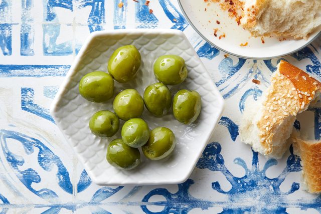 Castelvetrano olives in a white dish on blue and white background with pieces of bread nearby