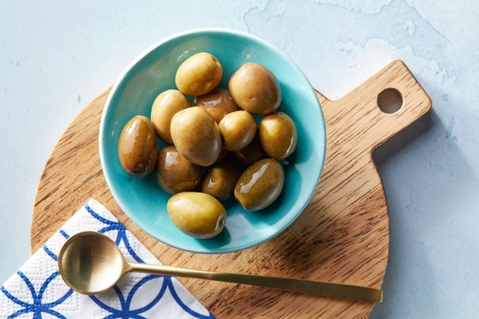 Mission olives in a small bowl on a cutting board on blue background