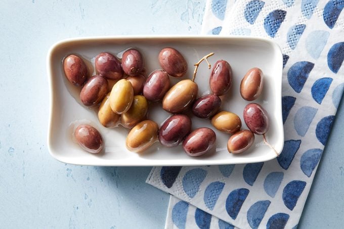 Nicoise olives in a dish on blue background with blue patterned napkins