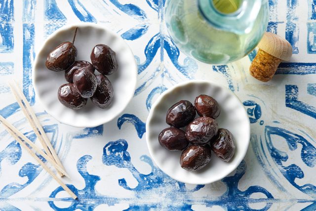 two small white bowls of Nyons olives on blue and white background with olive oil nearby