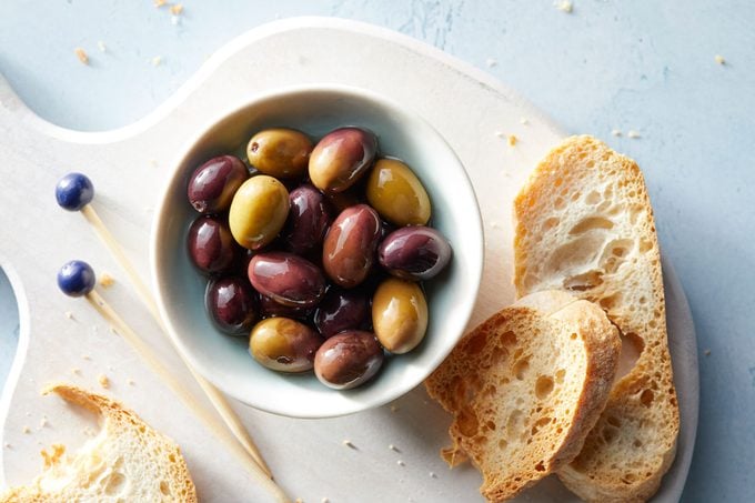 Taggiasca olives in a bowl on a cutting board with slices of bread