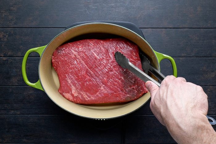 A person holding tongs to a piece of meat 