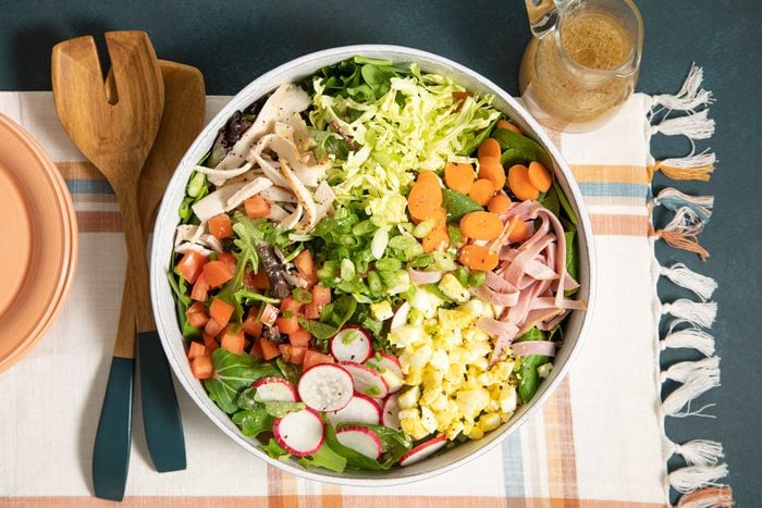 A bowl of salad with chicken, radishes, and carrots.