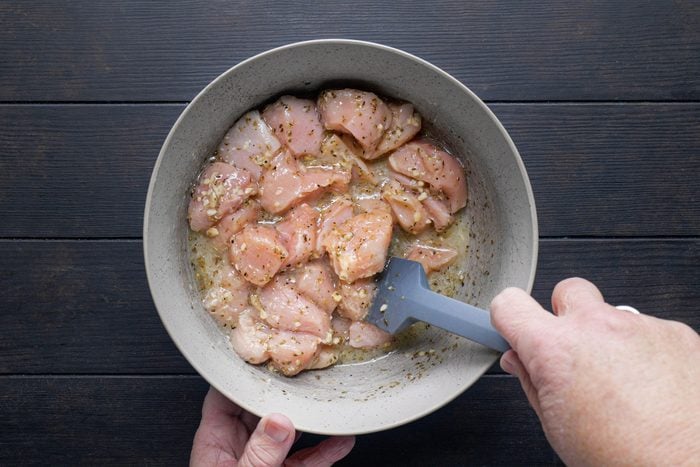 Chicken chunks lemon juice and other ingredients mixed in a large bowl with a spatula