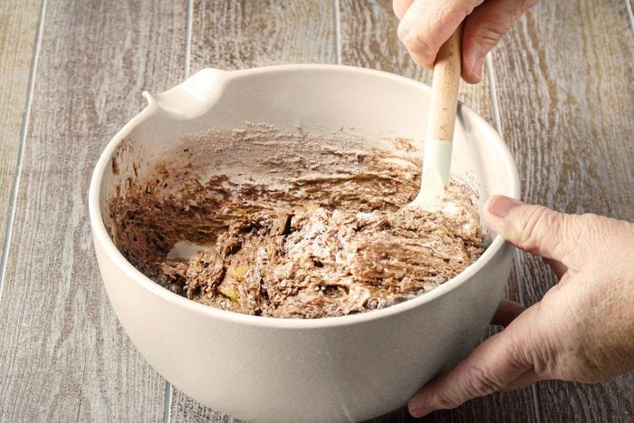 Combining the cocoa mixture with mashed bananas in a large bowl using a spatula
