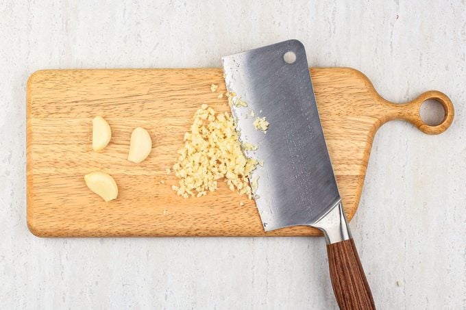 Chopped Garlic On The Wooden Chopping Board With Chopper Knife