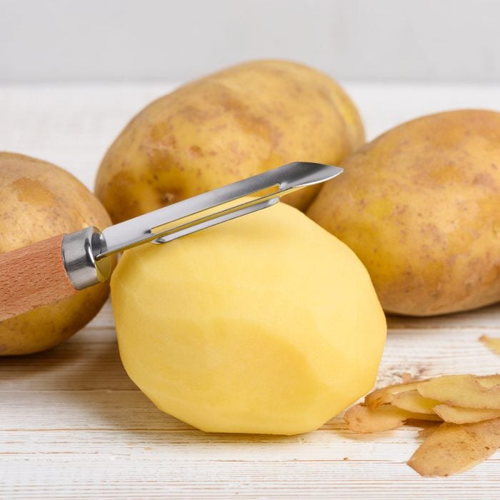 Raw peeled potato with vegetable peeler on wooden table