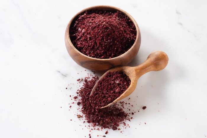 sumac spice in a small wooden bowl on a marble background