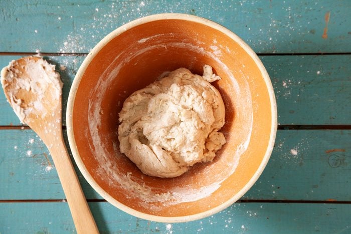 A bowl of dough with flour and a wooden spoon.