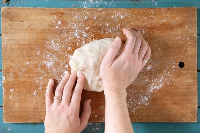 A woman's hands kneading dough on a wooden board.
