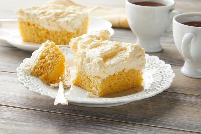 Orange cake on plate with spoon and hot beverage in cup