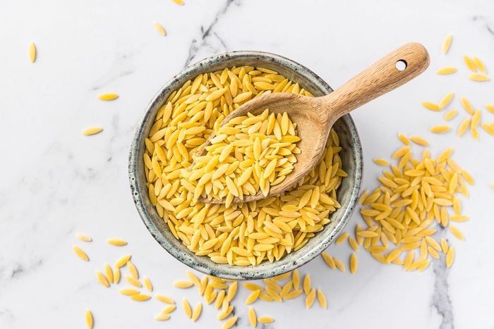 Raw Orzo Pasta (Risoni) In Bowl With Wooden Spoon On Marble Background