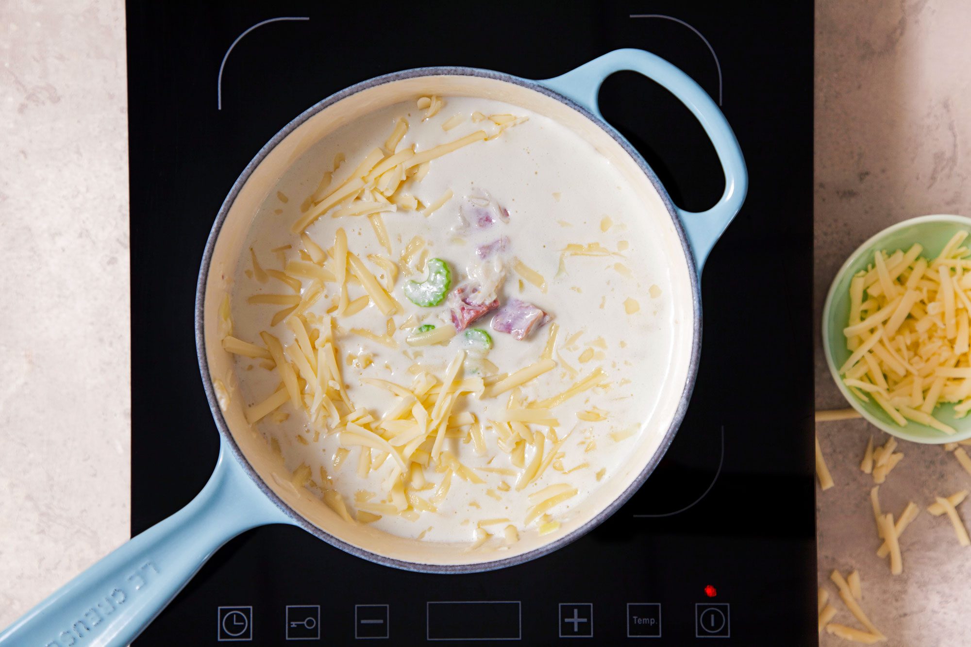 Sprinkled Cheese on Reuben Soup in A Saucepan on Induction Cooktop on A Marble Kitchen Top