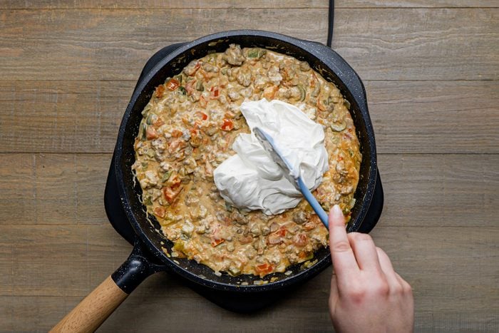 Adding the cream cheese in the sausage mixture in a skillet using a spatula