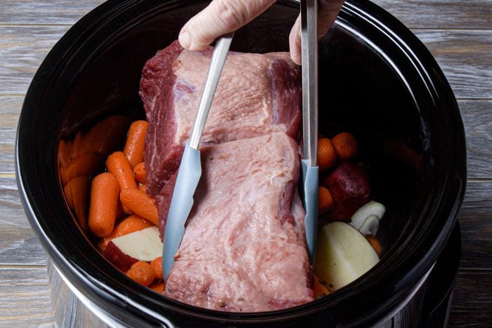 Placing brisket in a slow cooker along with other vegetables