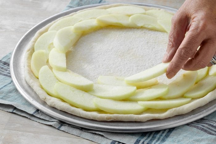 A person cutting apple slices into a pie crust