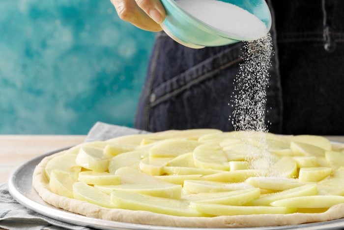 A person is sprinkling sugar on a apple tart