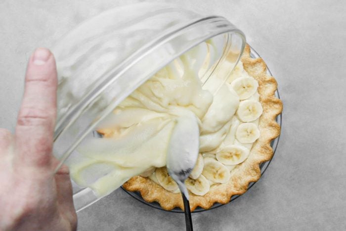 Pouring custard mix over arranged bananas on pie base