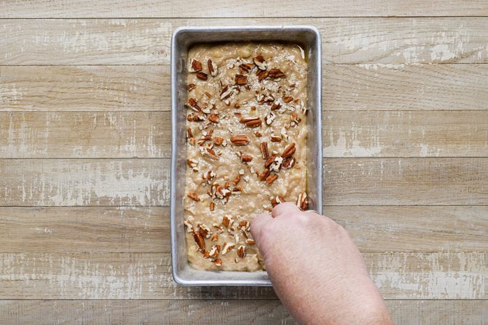 A hand sprinkling chopped pecans over banana bread batter in a loaf pan. 