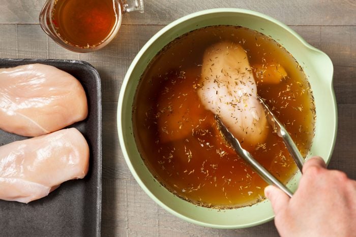 dipping chicken into a bowl full of brine, wooden background
