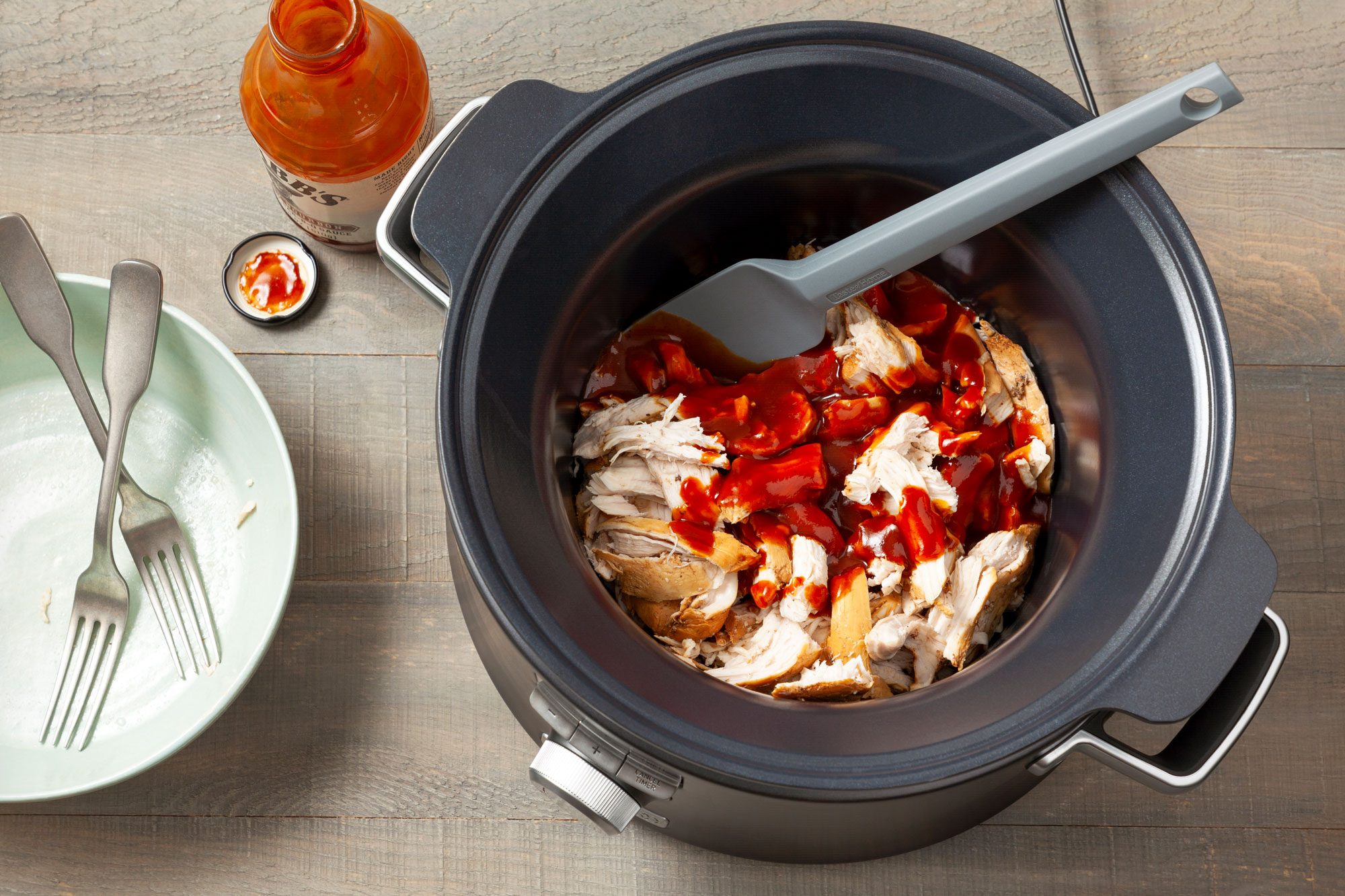 Chicken with Barbecue Sauce over it in a slow cooker on wooden surface