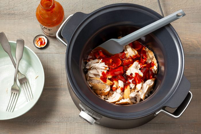 Chicken with Barbecue Sauce over it in a slow cooker on wooden surface