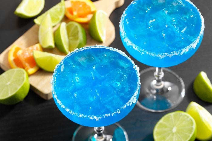 Blue Margarita glasses on black surface with fruits lying around
